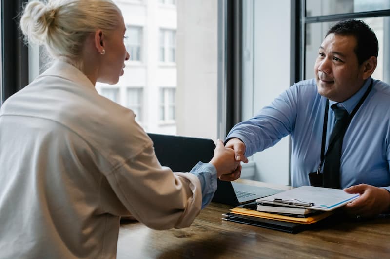 An Insurance agent shaking a womans hand while they sit opposite of a desk