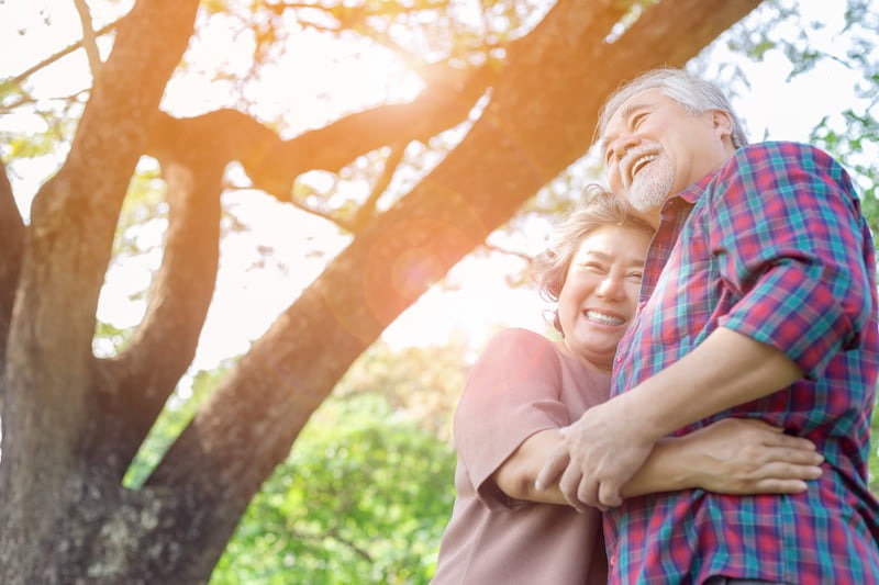 Elderly couple laughing and hugging under a tree
