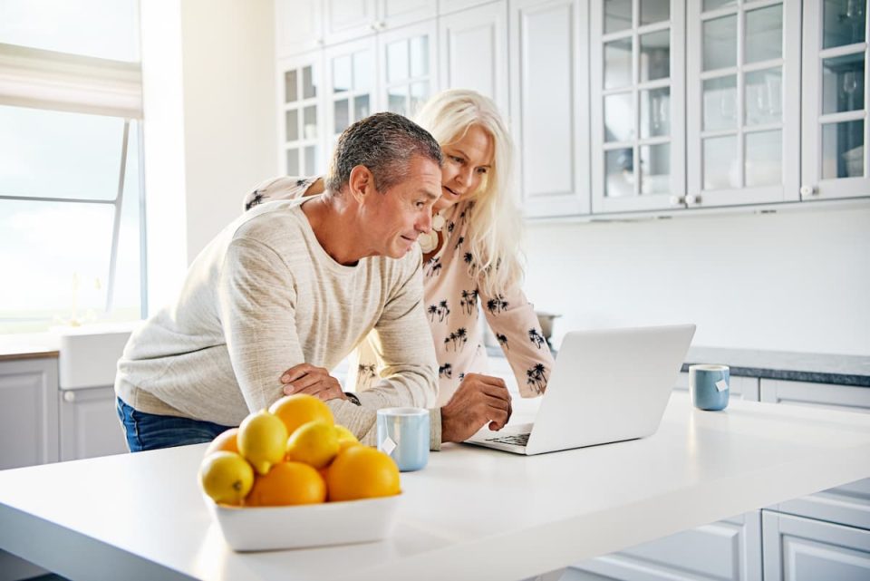 A couple leaning over their kitchen island looking at a laptop