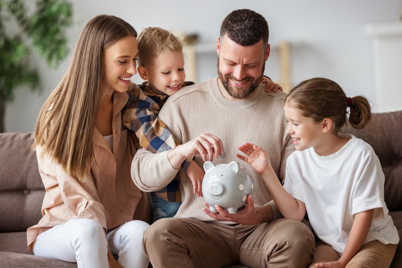 A young family sitting on a couch together while adding coins to a piggy bank
