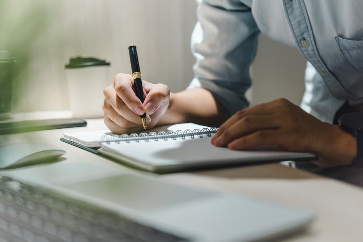 A pair of hands writing in a notebook with a pen