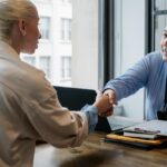 An Insurance agent shaking a womans hand while they sit opposite of a desk