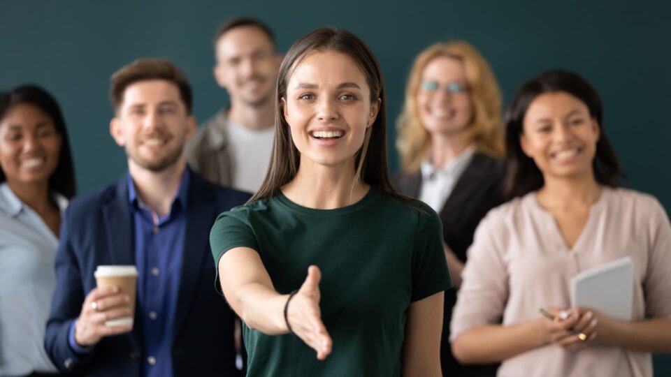 A group of smiling people with a woman in the center reaching out for a handshake