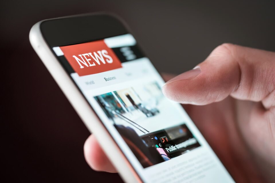 A close up shot of a hand holding a phone that is displaying a news website